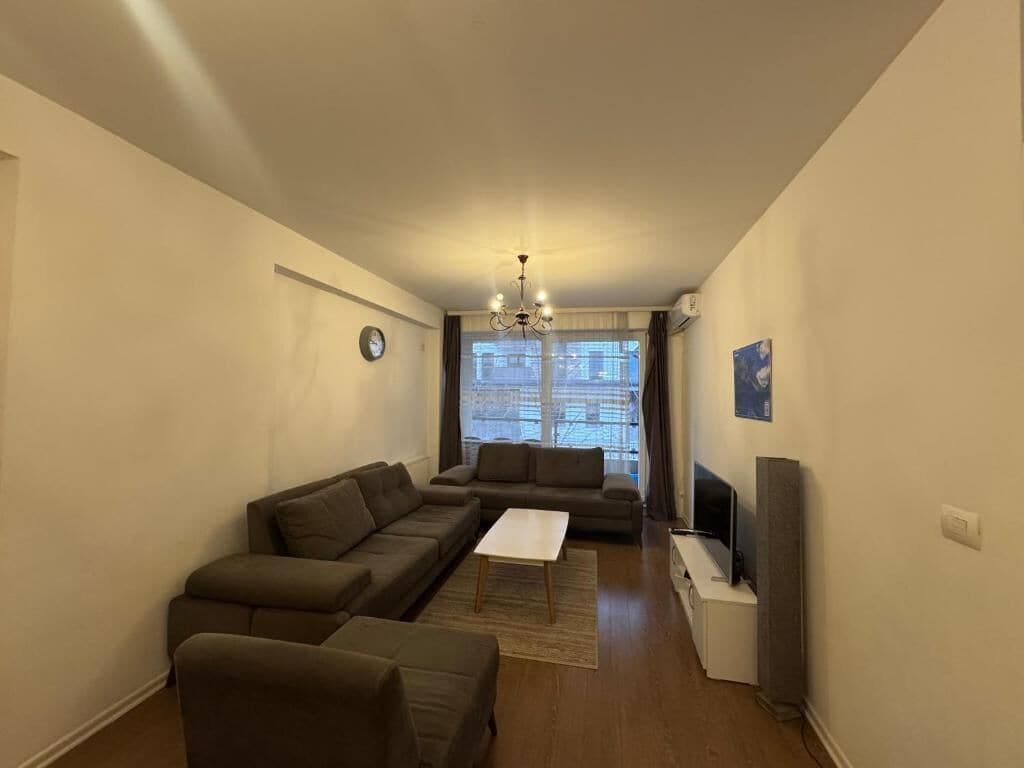 Un salón con sofá, mesa de centro, televisor y ventana con cortinas.