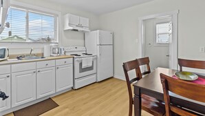 Una cocina compacta con armarios blancos, estufa, refrigerador y una mesa de comedor con sillas.