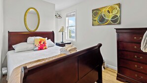 Un dormitorio con cama de madera, espejo, cómoda, ventana y un cuadro.