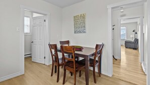 Un comedor con mesa y sillas de madera, un adorno en la pared y vista a otra habitación.