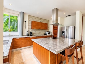 Eine moderne Küche mit Granit-Arbeitsplatten, Holzschränken, Edelstahlgeräten und einer großen Kücheninsel mit Barhocker.