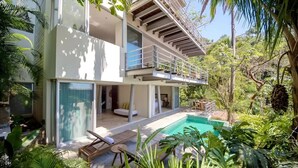 Ein modernes, zweistöckiges Haus mit Balkon, Swimmingpool und üppiger Bepflanzung.