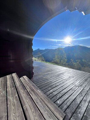 A wooden deck with a clear view of a mountainous landscape and the sun shining through an archway. - Chalet in Les Gets - Sleeps 9 - Breathtaking Views (Les Gets)