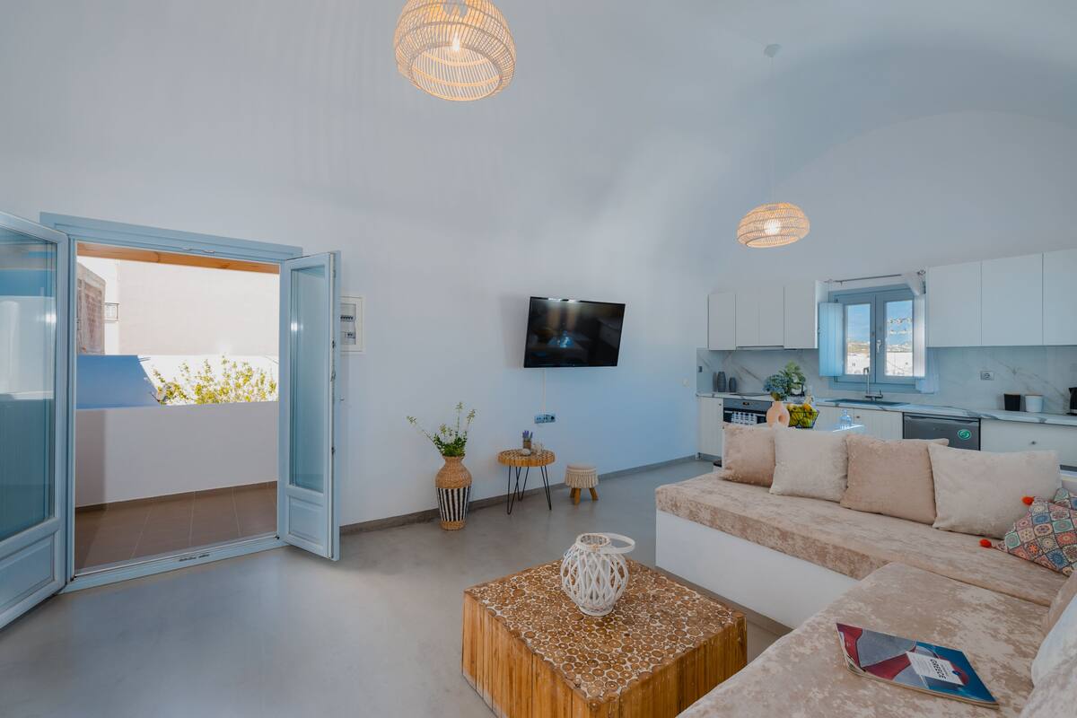 Una sala de estar moderna con un sofá, una mesa de centro y un televisor. Hay una zona de cocina con armarios y un ventanal.