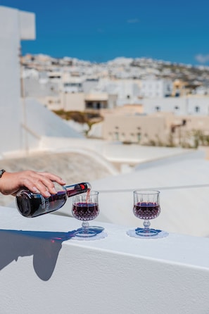 Eine Hand gießt Wein in ein Glas auf einem Balkon mit Stadtansicht im Hintergrund.