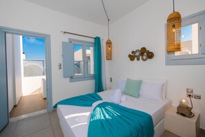 A bedroom with a bed, a bedside table with a lamp, a window with curtains, and a view of the outside. - Begi Luxury Villas (Santorini)