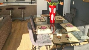 A modern dining area with a glass table, grey upholstered chairs, and a red vase with flowers. - Luxury modern 3 bed Penthouse apartment in Green Point near V&A Waterfront, CBD (Cape Town)