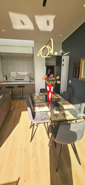 A modern dining area with a glass table, grey upholstered chairs, and a red vase with flowers. - Luxury modern 3 bed Penthouse apartment in Green Point near V&A Waterfront, CBD (Cape Town)