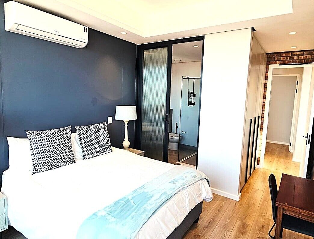 Une chambre à coucher comprenant un lit, une table de chevet, une lampe et un appareil de climatisation.