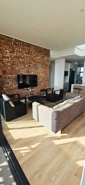 Una sala de estar moderna con pared de ladrillo, televisor de pantalla plana, sofá y mesa de centro.
