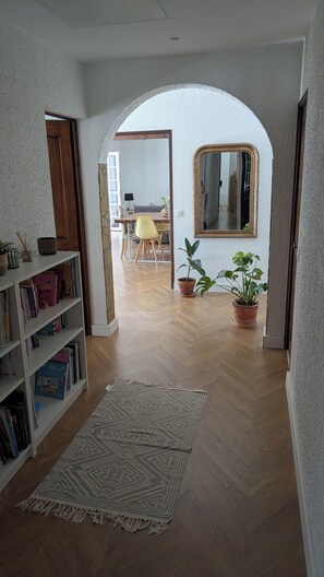 A hallway with a wooden floor, a bookshelf, a patterned rug, and two potted plants. - House with swimming pool in the heart of the Parc de la Sainte-Baume (La Roquebrussanne)