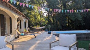 Une terrasse en bois avec des chaises longues, un hamac et une piscine.