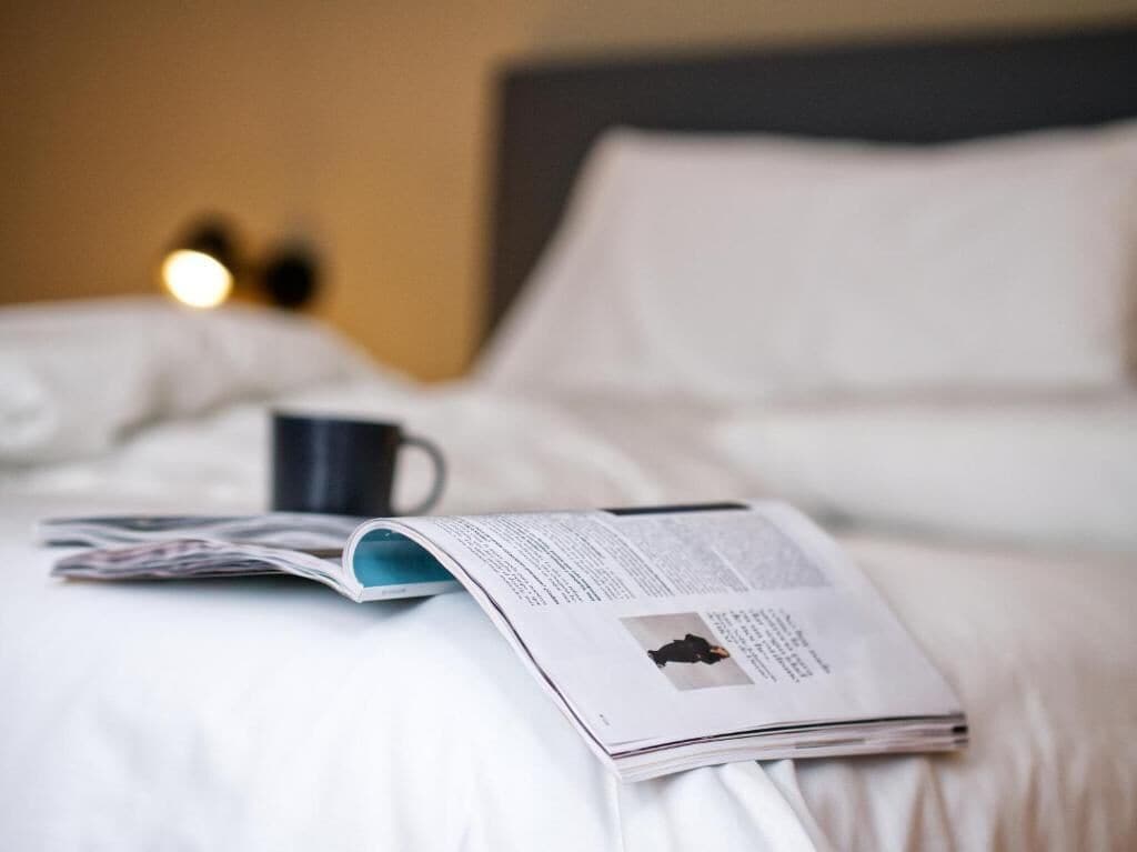 A bed with white bedding, a magazine, and a black mug.