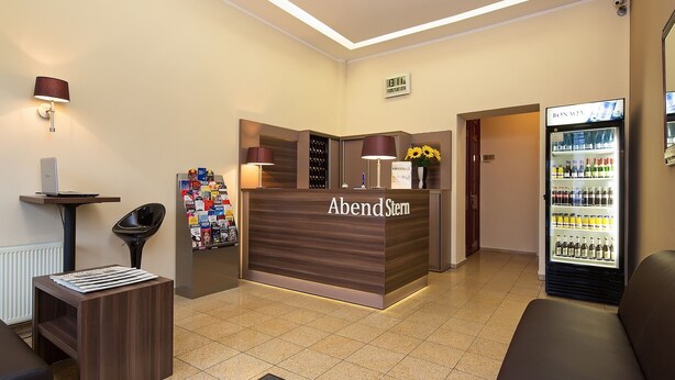 Un mostrador de recepción con un letrero que dice 'AbendStell', un refrigerador lleno de bebidas y una sala de estar con un sofá y una mesita.