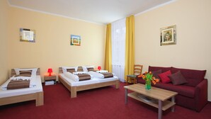 Habitación de hotel con dos camas individuales, un sofá rojo, una mesita de centro de madera y una alfombra roja.