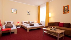 Habitación de hotel con dos camas individuales, un sofá, una silla roja, una mesa de madera y una lámpara.