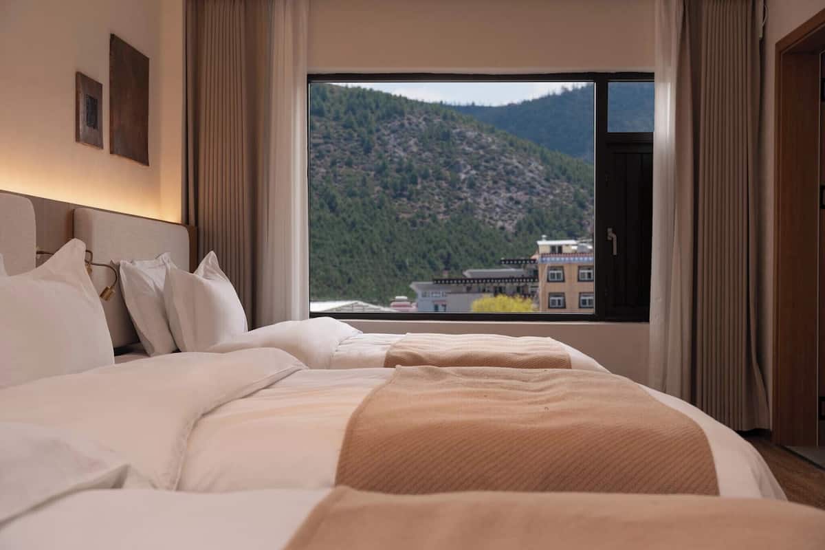 A hotel room with a large bed, a window with a mountain view, and a door.