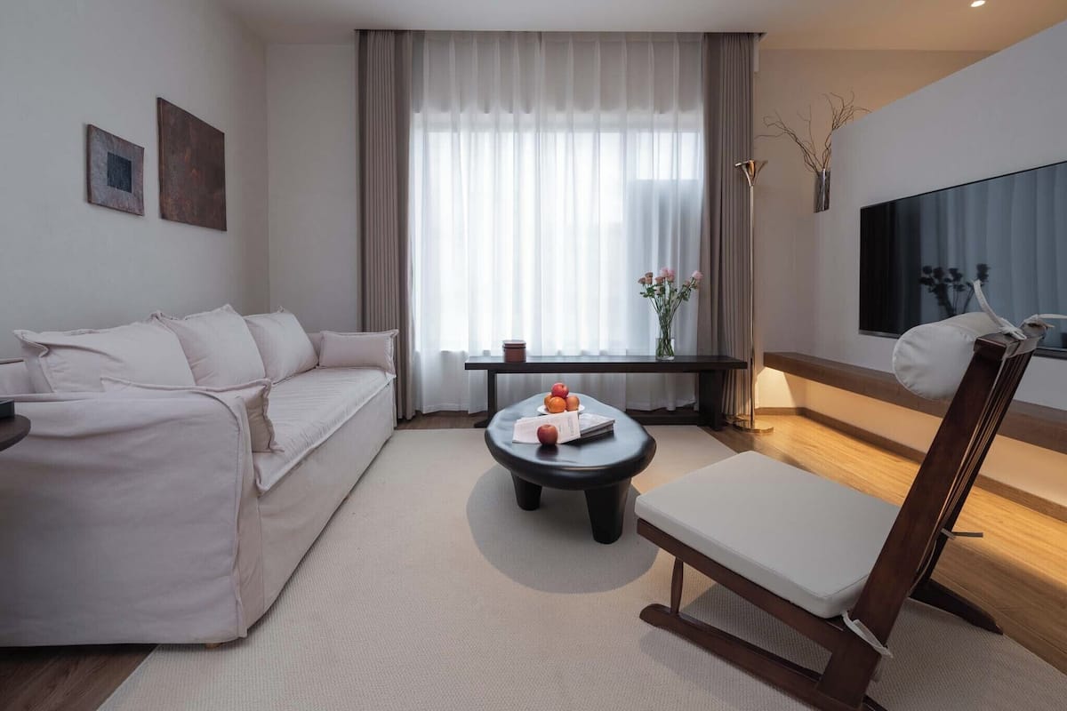 A modern living room with a sofa, a coffee table with fruit, a chair, a TV, and a window with curtains.