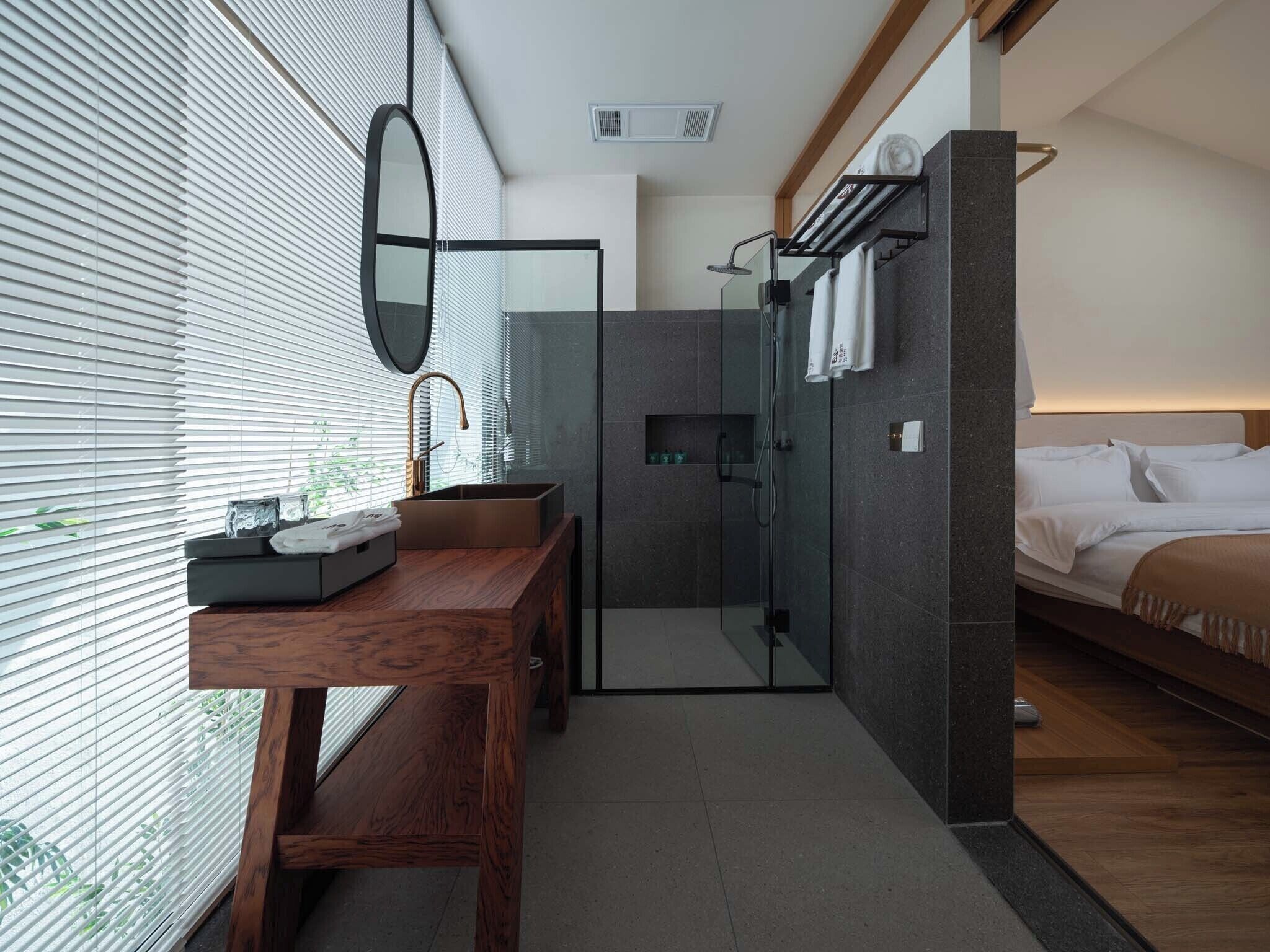 A modern bathroom with a glass shower enclosure, a wooden vanity, and a bed with a headboard.