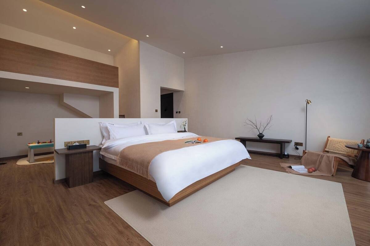 A modern bedroom with a large bed, bedside tables, a floor lamp, and a small seating area.