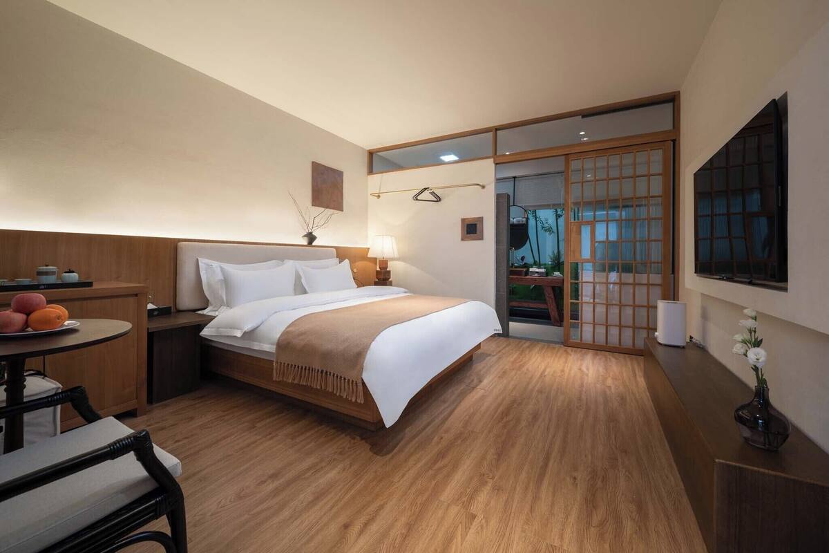 A hotel room with a bed, bedside table, chair, and a view through a sliding door.