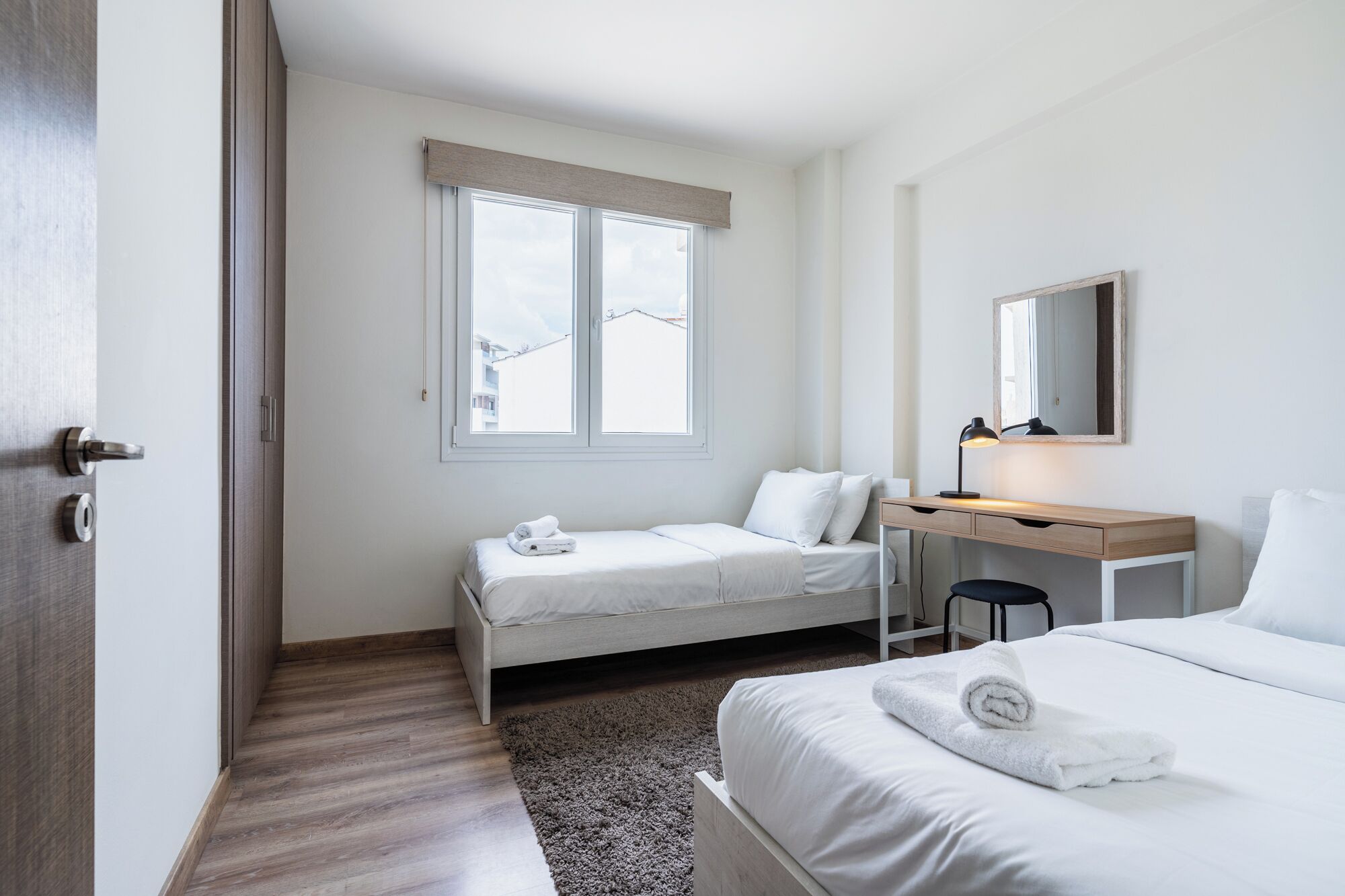 Une chambre d’hôtel avec un lit, un bureau et une chaise, une fenêtre donnant sur un paysage agréable et une porte.