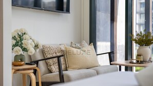 Ein modernes Wohnzimmer mit einer Couch, einem kleinen Tisch, einer Blumenvase und einem an der Wand befestigten Fernseher.