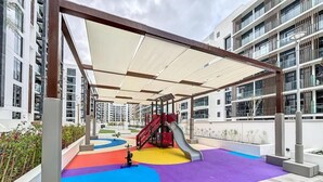 Ein Spielplatz mit Rutsche und Klettergerüst, umgeben von einem überdachten Bereich mit farbenfroher Spieloberfläche.