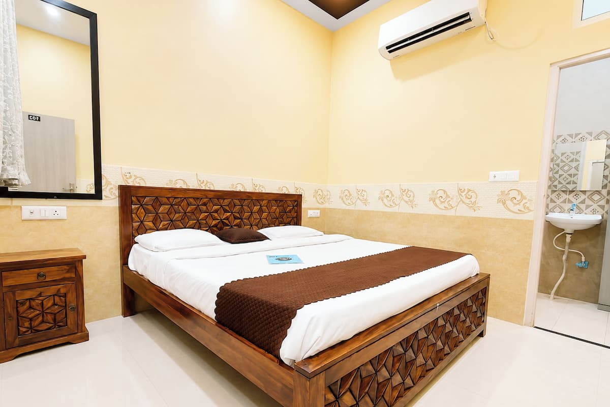 Habitación de hotel con cama de madera, mesita de noche, espejo y baño con lavamanos y espejo.