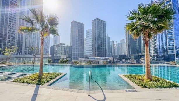 A swimming pool with palm trees, surrounded by high-rise buildings.