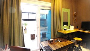 A room with a desk, chair, and a sliding glass door leading to an outdoor area. - Heritage Hotel (Changwon)