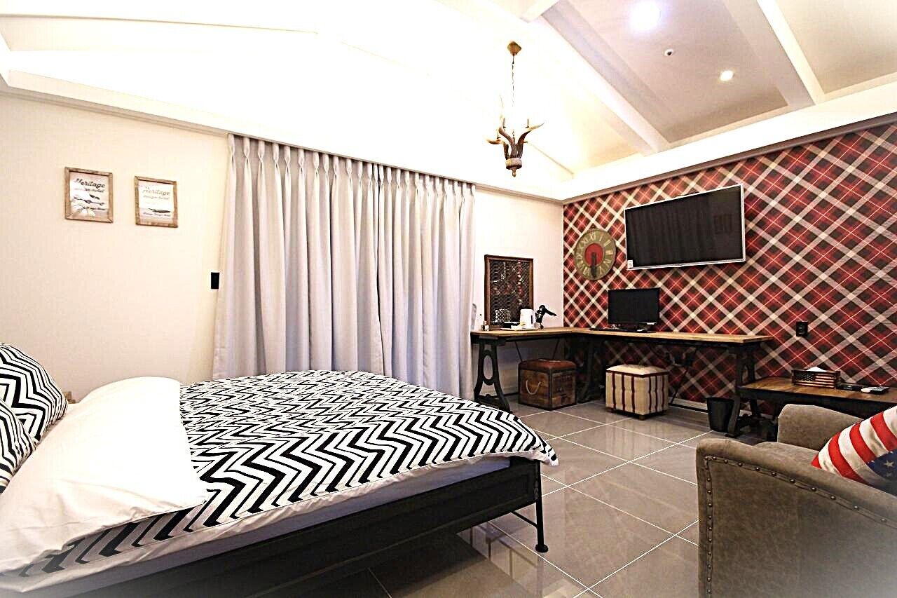 A bedroom with a bed, a desk, a chair, a television, and a patterned wall.