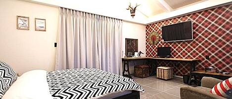 A bedroom with a bed, a desk, a chair, a television, and a patterned wall.