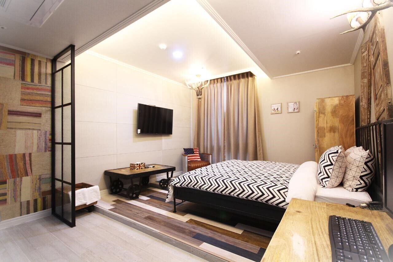 A bedroom with a bed, a desk with a keyboard, a TV, and a window with curtains.