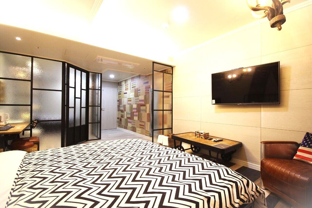 A hotel room with a bed, a TV, a desk, and a seating area.