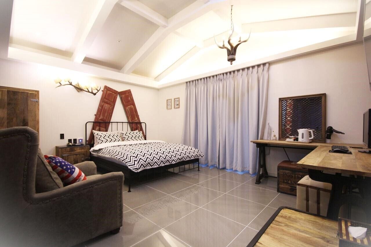 A bedroom with a bed, a desk, a chair, curtains, a chandelier, and a wall-mounted light fixture.