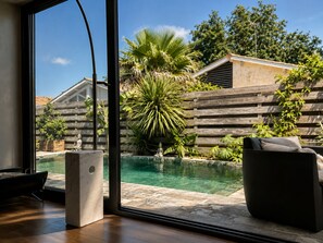 A modern interior with a large window overlooking a swimming pool, wooden deck, and outdoor furniture.