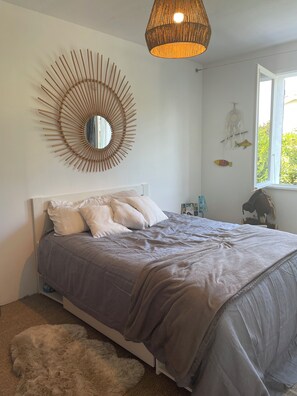 Ein Schlafzimmer mit einem Bett, einem runden Spiegel, einer Pendelleuchte, einem Fenster und Wanddekorationen.