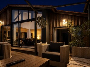 Ein moderner Außenbereich mit Patio, Korbmöbeln, einem Holztisch und einer Glastür zu einem Innenraum.