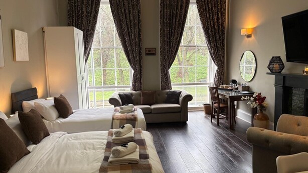 A hotel room with two beds, a sofa, a dining table, and a fireplace.