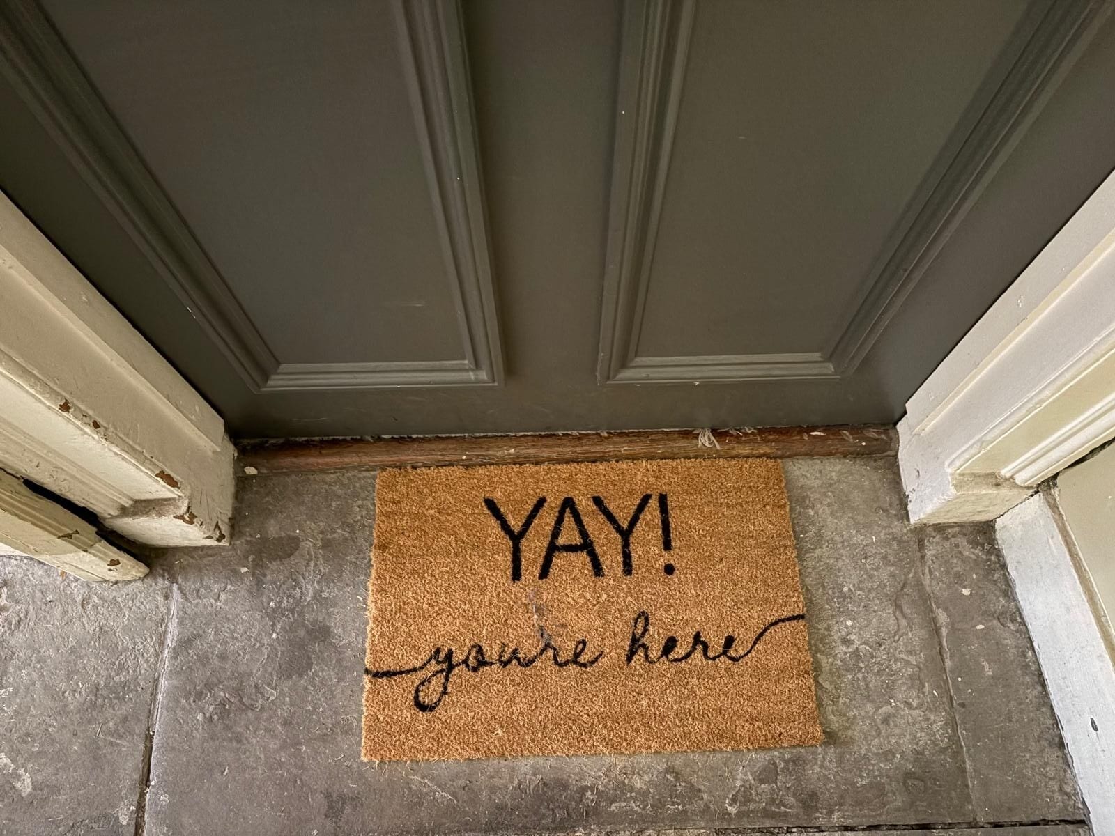A doormat with the words 'YAY! you're here' on a textured surface.