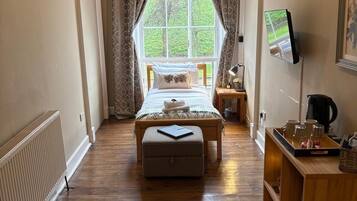 A bedroom with a bed, a bedside table, a TV, a radiator, and a window with curtains.