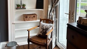 A room with a wooden chair, a white shelving unit with decorative items, a window with curtains, and a door with a brass handle.