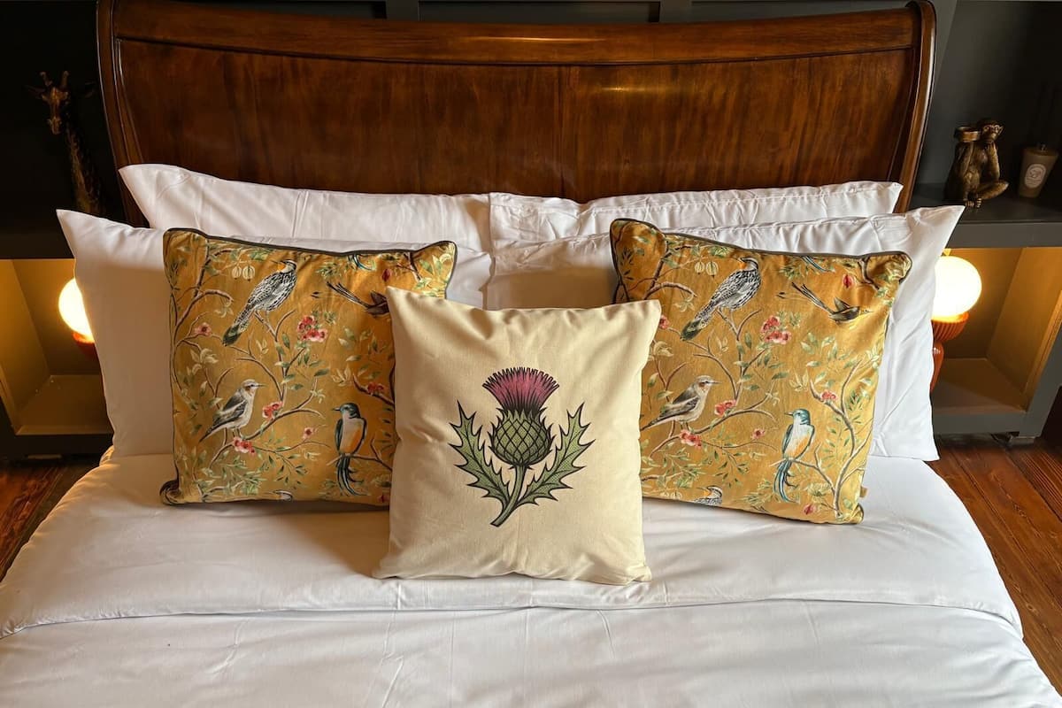 A bed with white linens, a wooden headboard, and decorative pillows with bird and floral patterns.