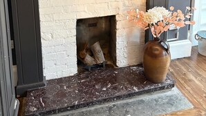 A fireplace with a TV above it, a vase with dried flowers, and a metal container on the mantel.