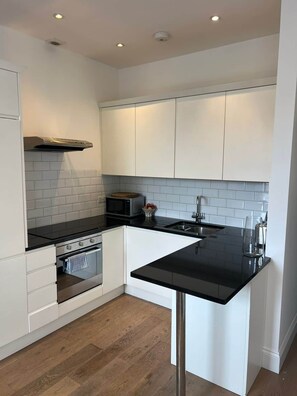 Eine moderne Küche mit weißen Schränken, einer schwarzen Arbeitsplatte und Holzboden.