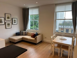 Ein Wohnzimmer mit einer Couch, einem Esstisch und einem fenster mit Vorhängen.
