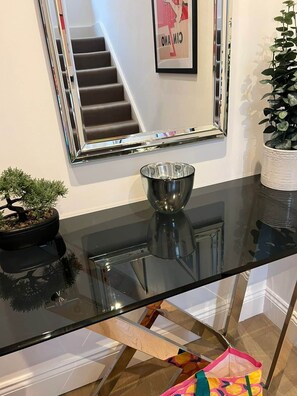 Ein modernes Interieur mit einem Glastisch, einem gerahmten Spiegel, einem Topfpflanzen und einer Treppe im Hintergrund.