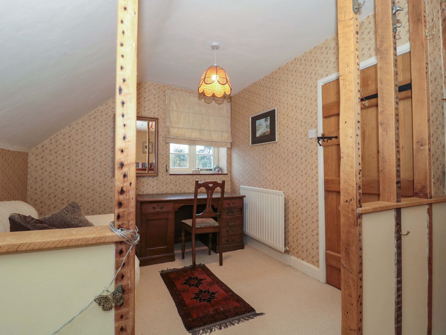 A bedroom with a wooden desk, a chair, a radiator, a window with a curtain, and a bed with a headboard.