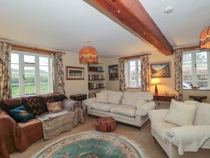A cozy living room with a fireplace, a large window with curtains, a bookshelf, and a patterned rug. - Tuxwell Lodge (Bridgwater)